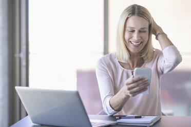 Glückliche Geschäftsfrau benutzt Handy im Büro - UUF17531