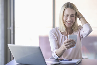Happy businesswoman using cell phone in office - UUF17531