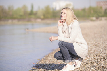 Smiling mature woman crouching at the riverside - UUF17544