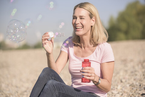 Glückliche reife Frau bläst Seifenblasen am Kieselstrand, lizenzfreies Stockfoto