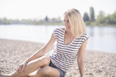 Smiling mature woman sitting at the riverside - UUF17594