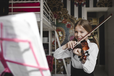 Lächelndes Mädchen spielt Geige und betrachtet den Notenständer zu Hause - EYAF00216
