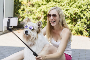 Happy woman taking a selfie with her dog wearing sunglasses - SHKF00806