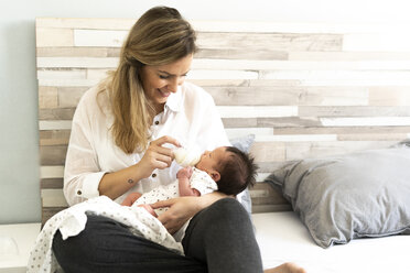 Mother bottle-feeding her newborn baby in bed - ERRF01305