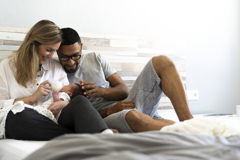 Glücklicher Vater und glückliche Mutter, die ihr neugeborenes Baby im Bett mit der Flasche füttern - ERRF01306