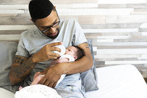 Father bottle-feeding his newborn baby in bed - ERRF01311