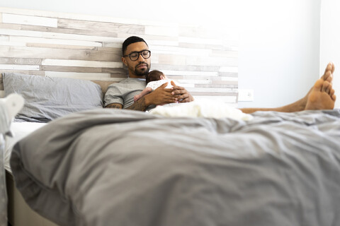 Vater hält sein neugeborenes Baby im Bett, lizenzfreies Stockfoto