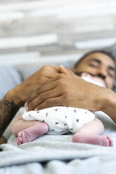 Man sleeping in bed holding his newborn baby - ERRF01321