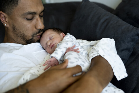Vater kuschelt mit neugeborenem Baby auf der Couch, lizenzfreies Stockfoto