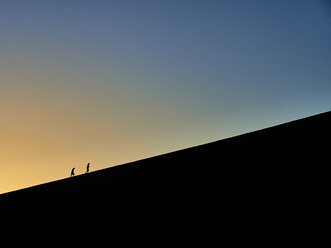 Silhouette von zwei Personen, die bei Sonnenaufgang auf Big Daddy wandern, Namib-Wüste, Namibia - VEGF00246