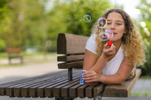 Junge Frau liegt auf einer Bank und bläst Seifenblasen, lizenzfreies Stockfoto