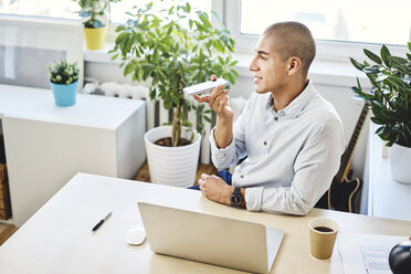 Porträt eines jungen Mannes, der im Büro zu Hause am Schreibtisch sitzt und telefoniert - BSZF01076