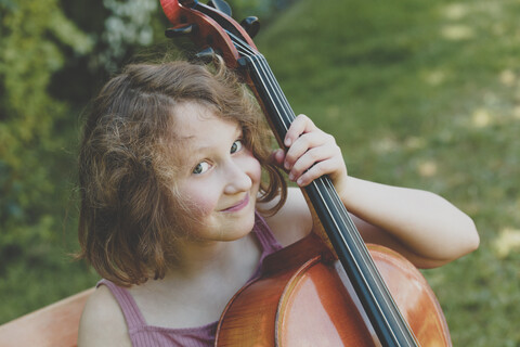 Ein lächelndes Mädchen mit einem Cello im Garten, lizenzfreies Stockfoto