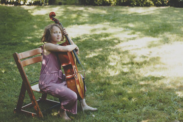 Ein Mädchen spielt im Garten Cello und schaut in die Kamera - IHF00029