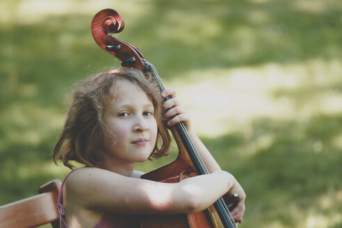 Ein Mädchen spielt im Garten Cello und schaut in die Kamera - IHF00030