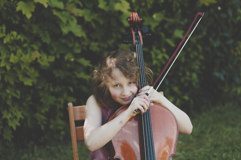 Ein Mädchen spielt im Garten Cello und schaut in die Kamera - IHF00031