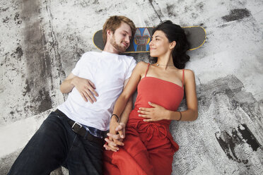 Mixed Race couple laying on rooftop with skateboard - BLEF03663