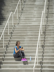 Kaukasische Frau sitzt auf einer Treppe und schreibt eine SMS auf ihrem Handy - BLEF03672