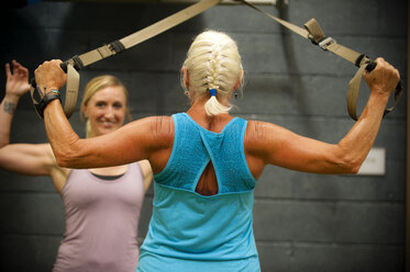 Trainer assisting older woman working out in gymnasium - BLEF03701