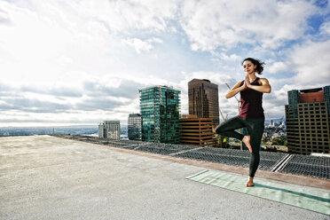 Kaukasische Frau macht Yoga auf dem Dach einer Stadt - BLEF03833