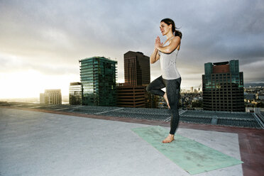 Kaukasische Frau macht Yoga auf dem Dach einer Stadt - BLEF03845