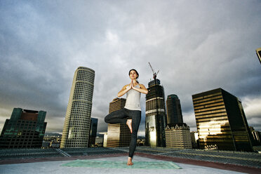 Kaukasische Frau macht Yoga auf dem Dach einer Stadt - BLEF03846