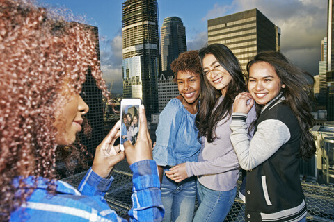 Stylish woman photographing friends on urban rooftop with cell phone stock photo