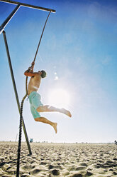 Kaukasischer Mann klettert an einem Seil am Strand - BLEF03858
