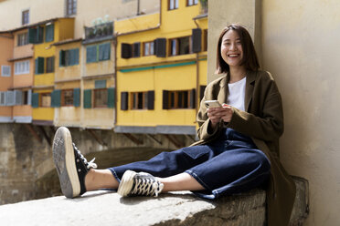 Italien, Florenz, glückliche junge Frau, die sich auf einer Mauer in der Stadt ausruht - FMOF00614