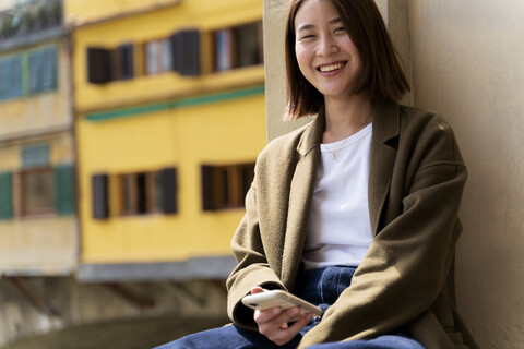 Italien, Florenz, glückliche junge Frau mit Smartphone beim Ausruhen in der Stadt, lizenzfreies Stockfoto