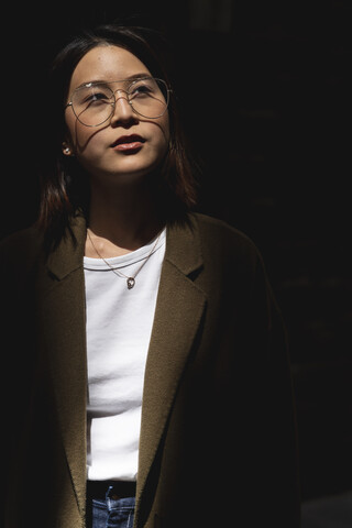 Porträt einer jungen Frau mit Brille im Sonnenlicht, die sich umschaut, lizenzfreies Stockfoto