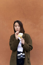 Junge Frau isst eine Eiswaffel an einer orangenen Wand - FMOF00631