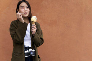 Junge Frau isst eine Eiswaffel an einer orangenen Wand - FMOF00633
