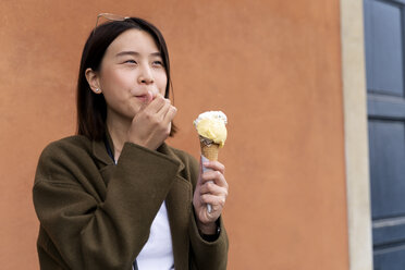 Junge Frau isst eine Eiswaffel an einer orangenen Wand - FMOF00634