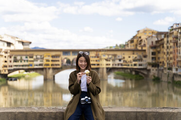 Italy, Florence, young tourist woman eating an ice cream cone at at Ponte Vecchio - FMOF00638