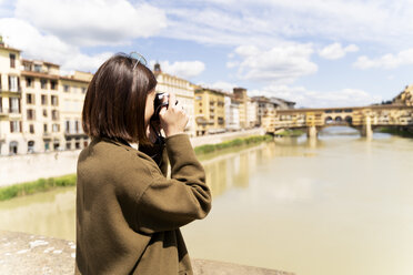 Italy, Florence, young tourist woman taking pictures at Ponte Vecchio - FMOF00640