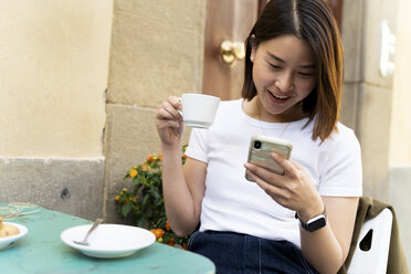 Italien, Florenz, junge Frau, die in einem Straßencafé ihr Handy benutzt - FMOF00652