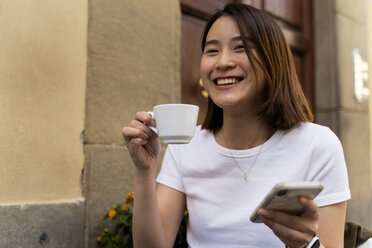 Italien, Florenz, glückliche junge Frau mit Handy in einem Straßencafé - FMOF00653