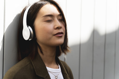Entspannte junge Frau mit geschlossenen Augen, die mit Kopfhörern Musik hört - FMOF00658