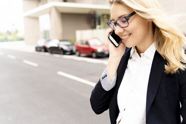 Smiling young businesswoman on the phone crossing street - FMOF00670