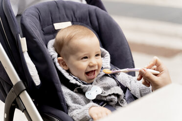 Mutter füttert lachenden kleinen Jungen im Kinderwagen - FMOF00675