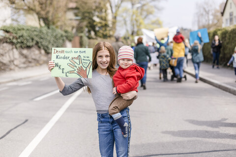 Mädchen mit Baby auf dem Arm hält ein Plakat auf einer Demonstration für den Umweltschutz, lizenzfreies Stockfoto