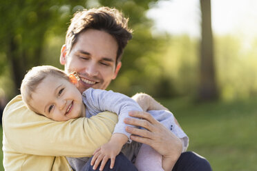 Porträt eines glücklichen Kleinkindes, das mit seinem Vater in einem Park kuschelt - DIGF07058