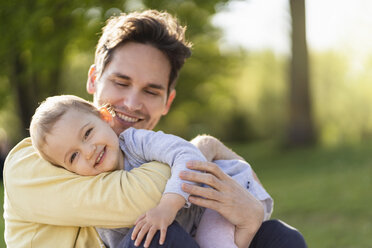 Portrait of happy toddler girl cuddling with her father in a park - DIGF07058