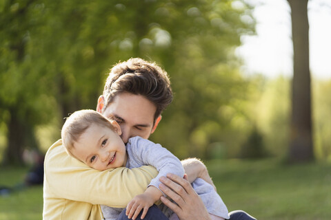 Porträt eines glücklichen Kleinkindes, das mit seinem Vater in einem Park kuschelt, lizenzfreies Stockfoto