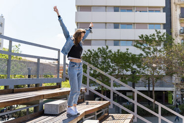 Young woman with raised arms standing on grandstand in Barcelona - AFVF02947