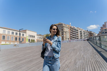 Junge Frau mit Smartphone auf einer Fußgängerbrücke in Barcelona - AFVF02954