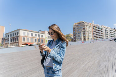 Junge Frau mit Smartphone auf einer Fußgängerbrücke in Barcelona - AFVF02955