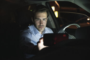 Young man using cell phone in car at night - UUF17600