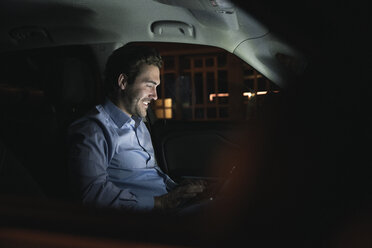 Lächelnder junger Mann mit Laptop im Auto bei Nacht - UUF17603
